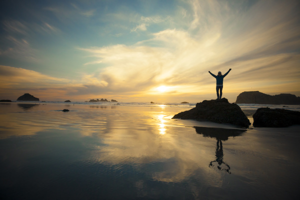 A silhouetted woman is reflected in the sand on Bandon Beach by Aurora Photos